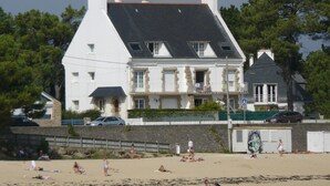 En stor hvid bygning med et stejlt tag og flere skorstene, beliggende nær en strand med solbadere.