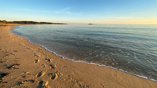 En strand med fodspor i sandet og et roligt hav.