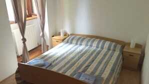 Una cama individual con colcha a rayas, cabecera de madera, mesita de noche con lámpara y ventana con cortinas.