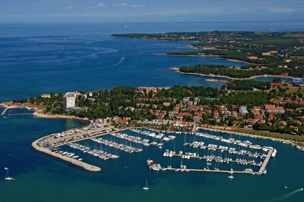 An aerial view of a coastal town with a marina filled with boats, surrounded by residential buildings and greenery.