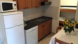 Une cuisine compacte équipée d’un réfrigérateur, d’un four à micro-ondes, d’une cuisinière et de meubles de rangement en bois.