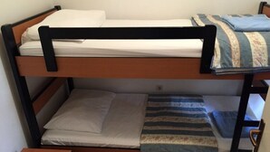 Un lit superposé à deux niveaux, chaque niveau étant équipé d’un matelas et d’oreillers. Une table de chevet en bois, dotée d’un tiroir, se trouve sous le lit du bas.