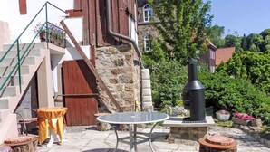 A stone patio with a round table and stools, a wooden staircase, and a black grill.