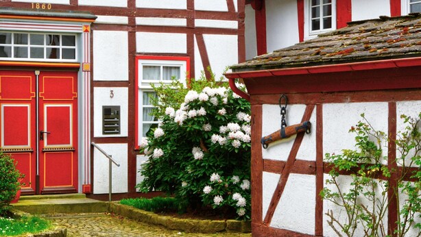 A traditional half-timbered building with a red door and white walls, number 3, and a small garden with white flowers.