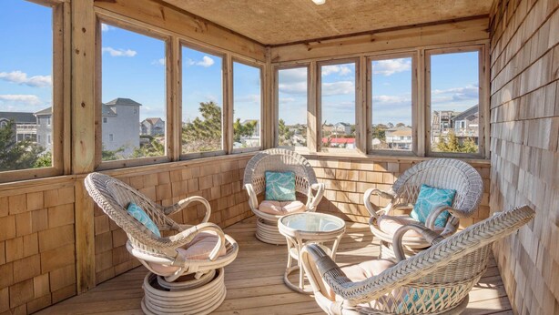Un espacio de estar techado al aire libre con sillas de mimbre y una mesa de vidrio, con vistas a un barrio residencial.
