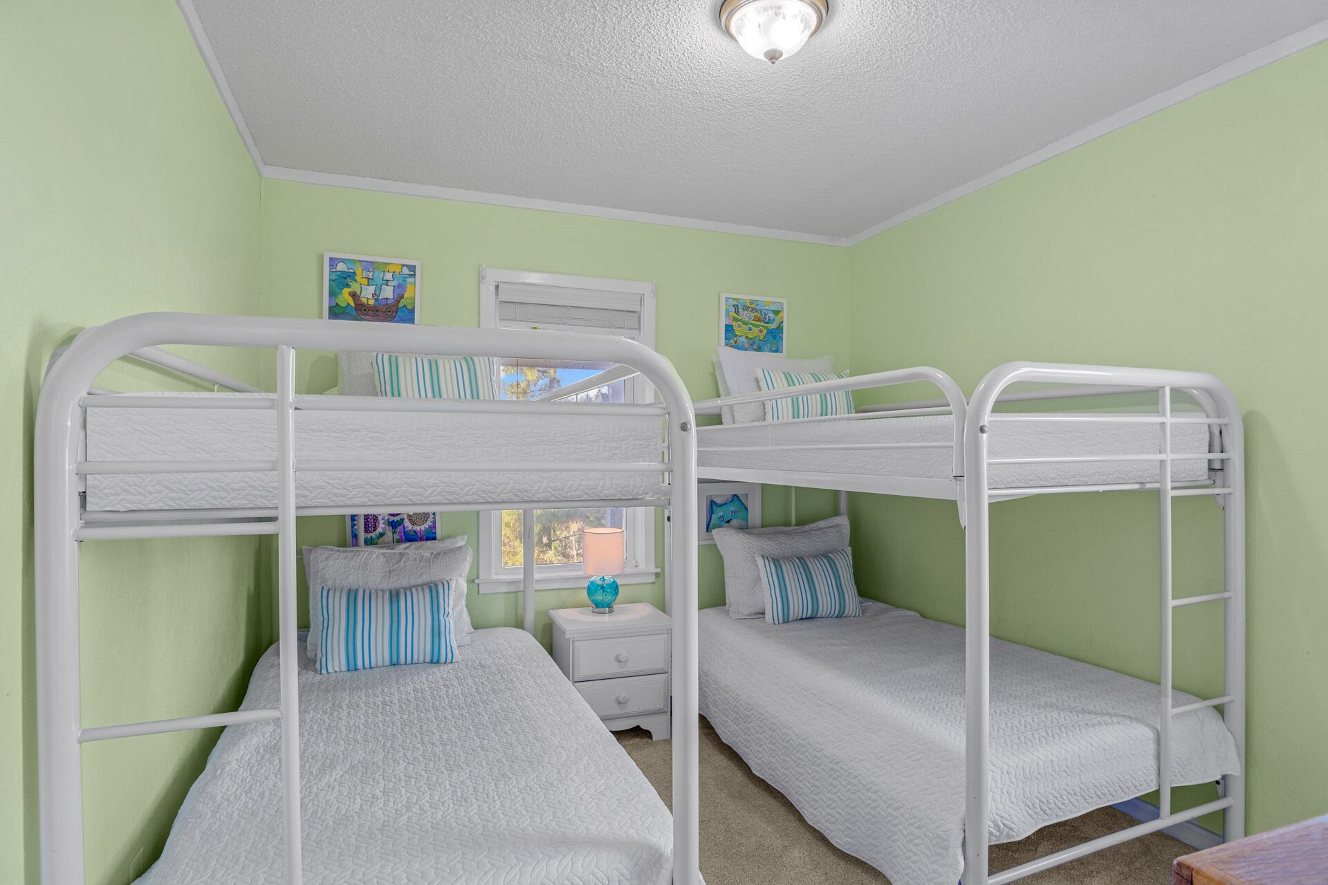A bunk bed room with a white metal frame, green walls, and a window with a view.