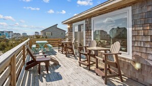 Una terraza de madera con mobiliario exterior, incluyendo mesas y sillas, con vistas a una zona residencial.