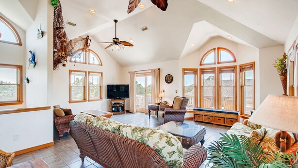 A spacious living room with a large sofa, a television, and a ceiling fan. - Oceanview Home in Salvo with Hot Tub, Game Room, Grill, Beach Nearby (Salvo)