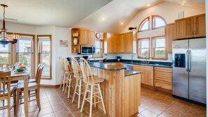 A spacious kitchen with wooden cabinets, a stainless steel refrigerator, and a large island with bar stools. - Oceanview Home in Salvo with Hot Tub, Game Room, Grill, Beach Nearby (Salvo)
