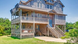 A two-story wooden house with a balcony, a front porch, and a staircase leading to the second floor. - Oceanview Home in Salvo with Hot Tub, Game Room, Grill, Beach Nearby (Salvo)