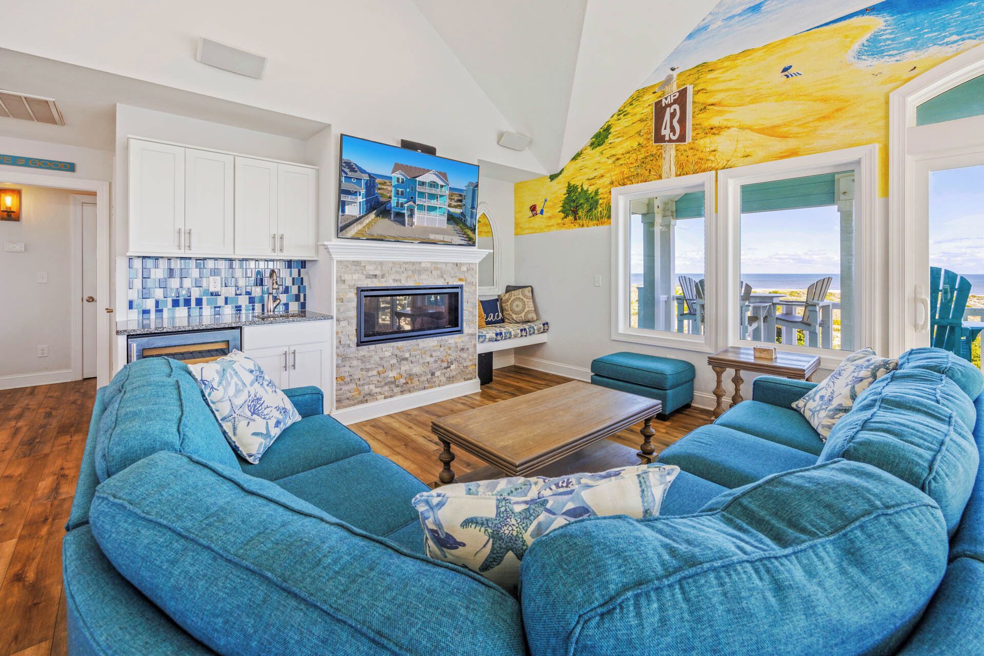 A living room with a large blue sofa, a fireplace, and a view of the beach.