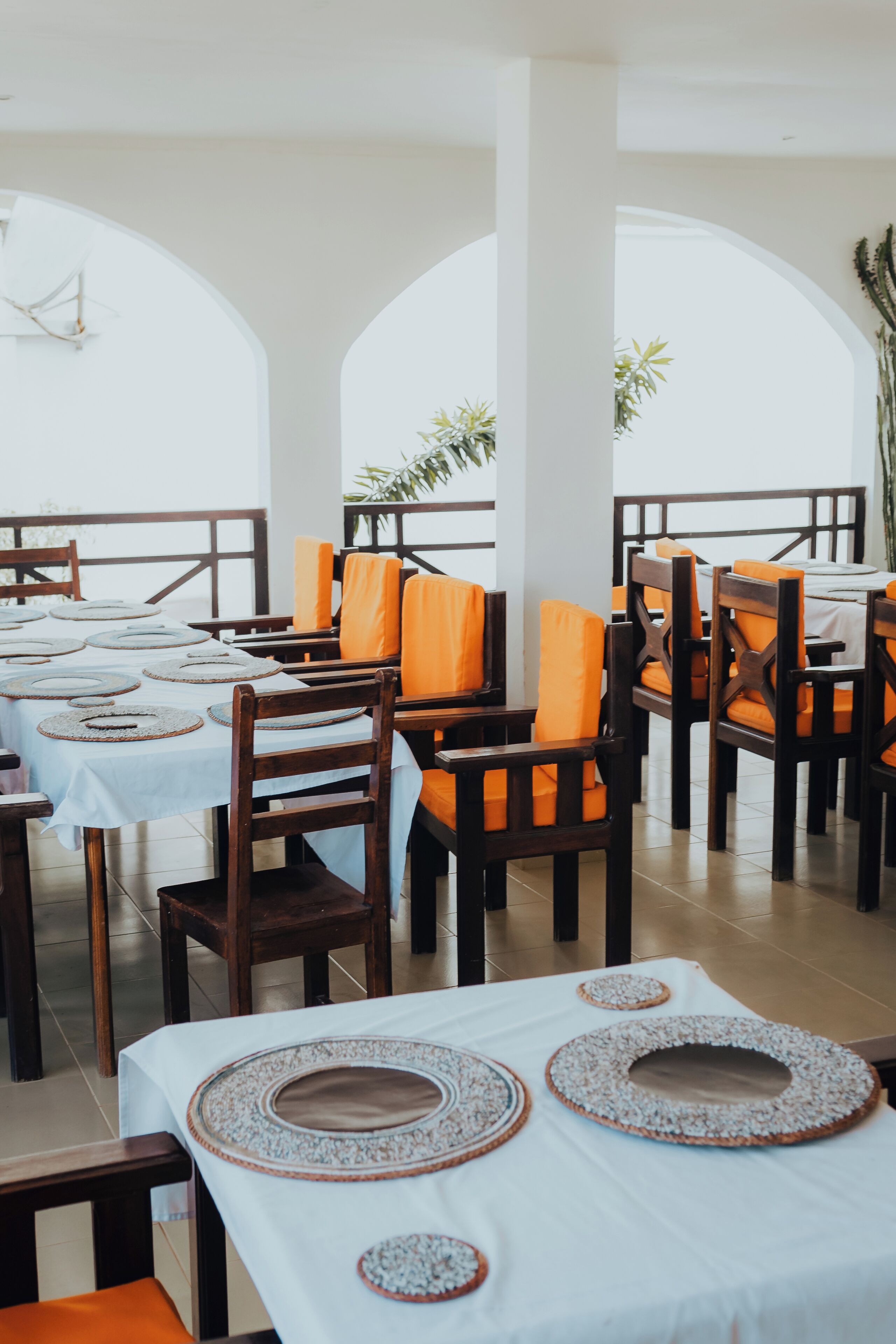 A restaurant with wooden tables and orange cushioned chairs, white tablecloths, and decorative plates.