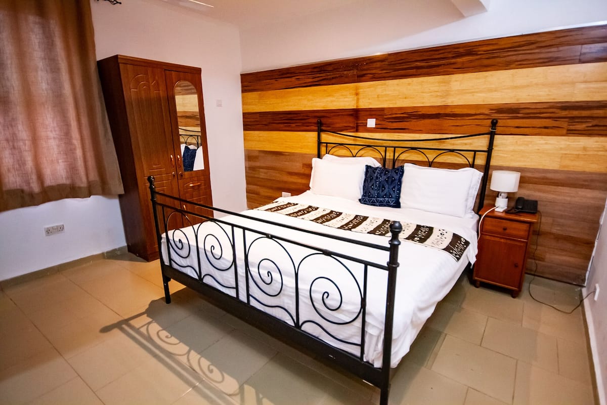 Een slaapkamer met een bed, een houten garderobe, nachtkastje en een spiegel.