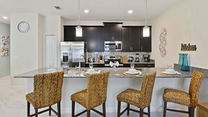 Una cocina moderna con gabinetes oscuros, electrodomésticos de acero inoxidable y una isla central con taburetes de bar.