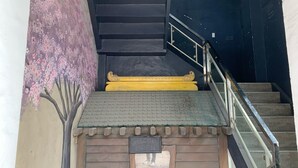 A staircase with a handrail, a wooden wall with a cherry blossom mural, and a sign with a welcome message. - Chiasti Capsule Hostel - Adults Only (Cebu City)