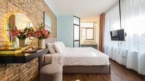 Un dormitorio moderno con pared de ladrillo, una cama grande, una mesita de noche con espejo y un televisor montado en la pared.
