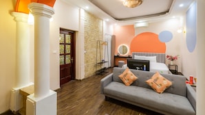 Habitación de hotel moderna con sofá gris, cama con un espejo grande, pared de piedra y suelo de madera.