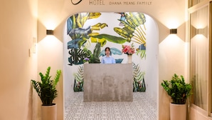 Zona de recepción con un mural de temática tropical, un mostrador de recepción y plantas en macetas.