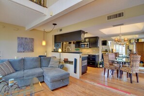 A modern living room with a grey sectional sofa, a glass coffee table, and a dining area with patterned chairs.