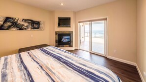 Ein Schlafzimmer mit einem großen Bett, einem Kamin, einem Fernseher und einer Glastür zum Balkon mit Blick auf den Strand.
