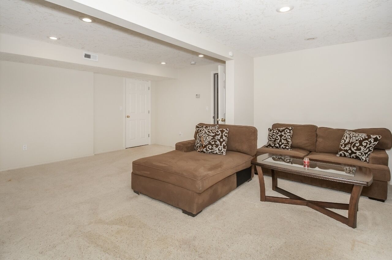 A living room with a brown sectional sofa, a glass coffee table, and a carpeted floor.