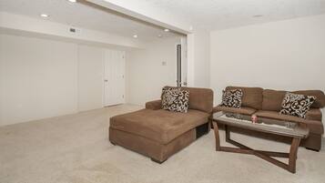 A living room with a brown sectional sofa, a glass coffee table, and a carpeted floor.