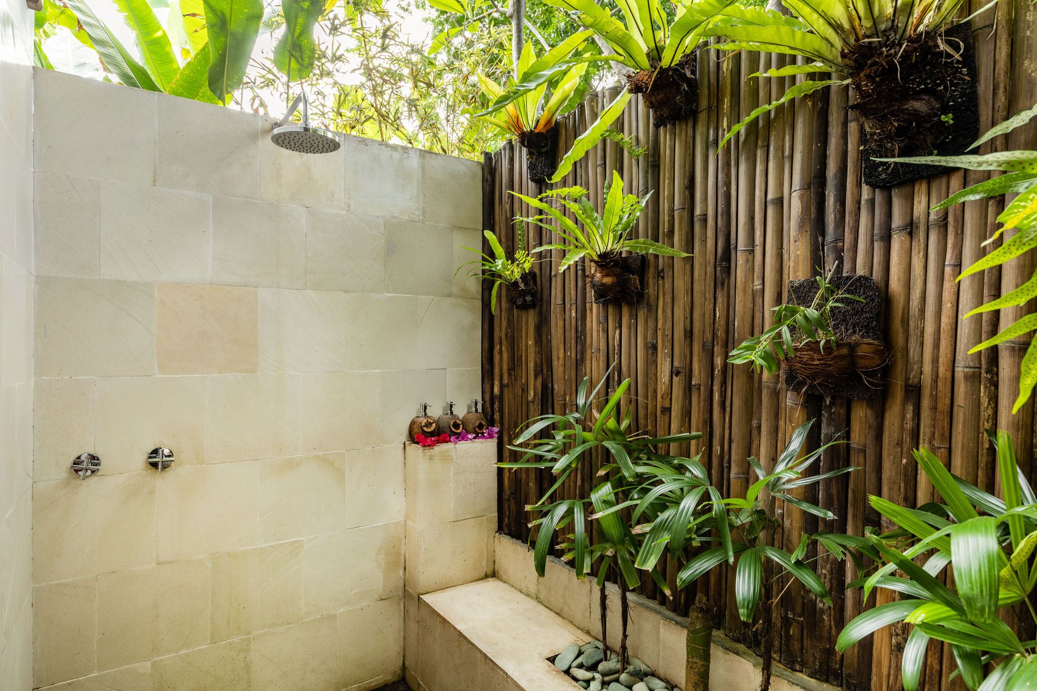 A shower area with stone tiles, a bamboo wall, and various potted plants.