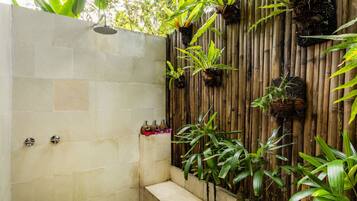 A shower area with stone tiles, a bamboo wall, and various potted plants.