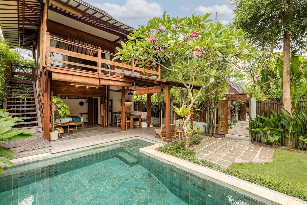 A two-story wooden house with a swimming pool and outdoor seating area.
