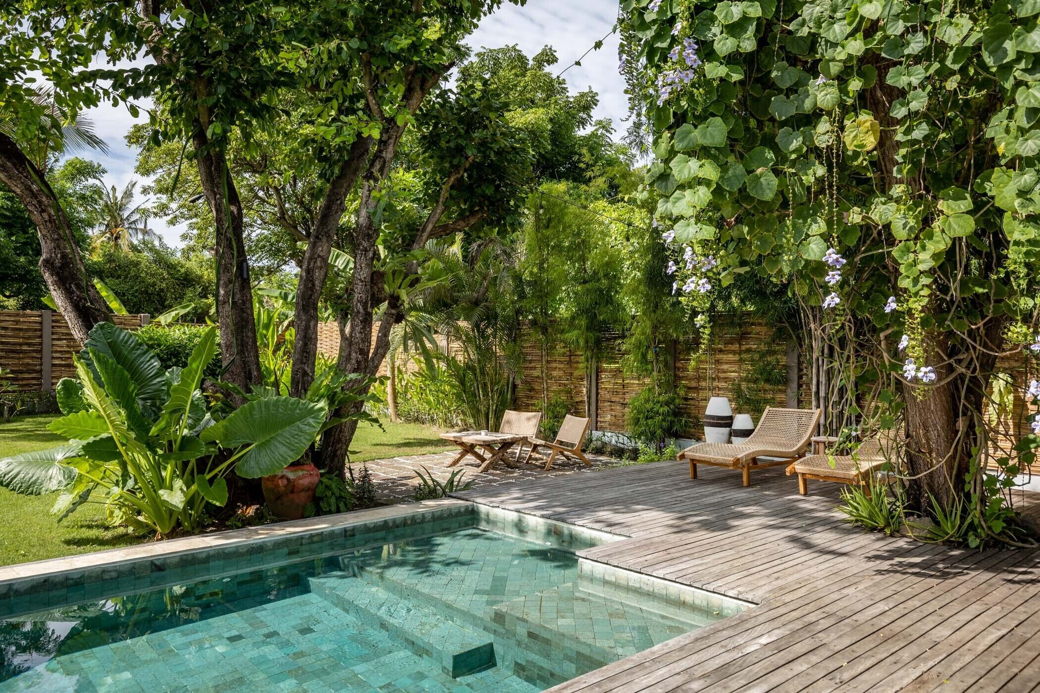 A wooden deck with a swimming pool, surrounded by lush greenery and trees.