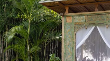 Duas crianças brincando em um cobertor em um jardim com uma estrutura de madeira e uma grande planta em vaso.