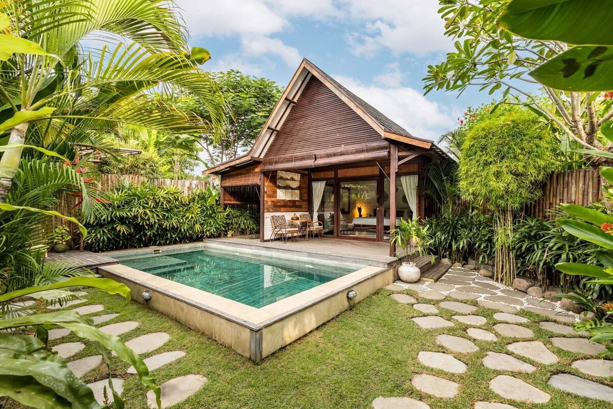 A wooden house with a swimming pool, surrounded by lush greenery and stone pathways.