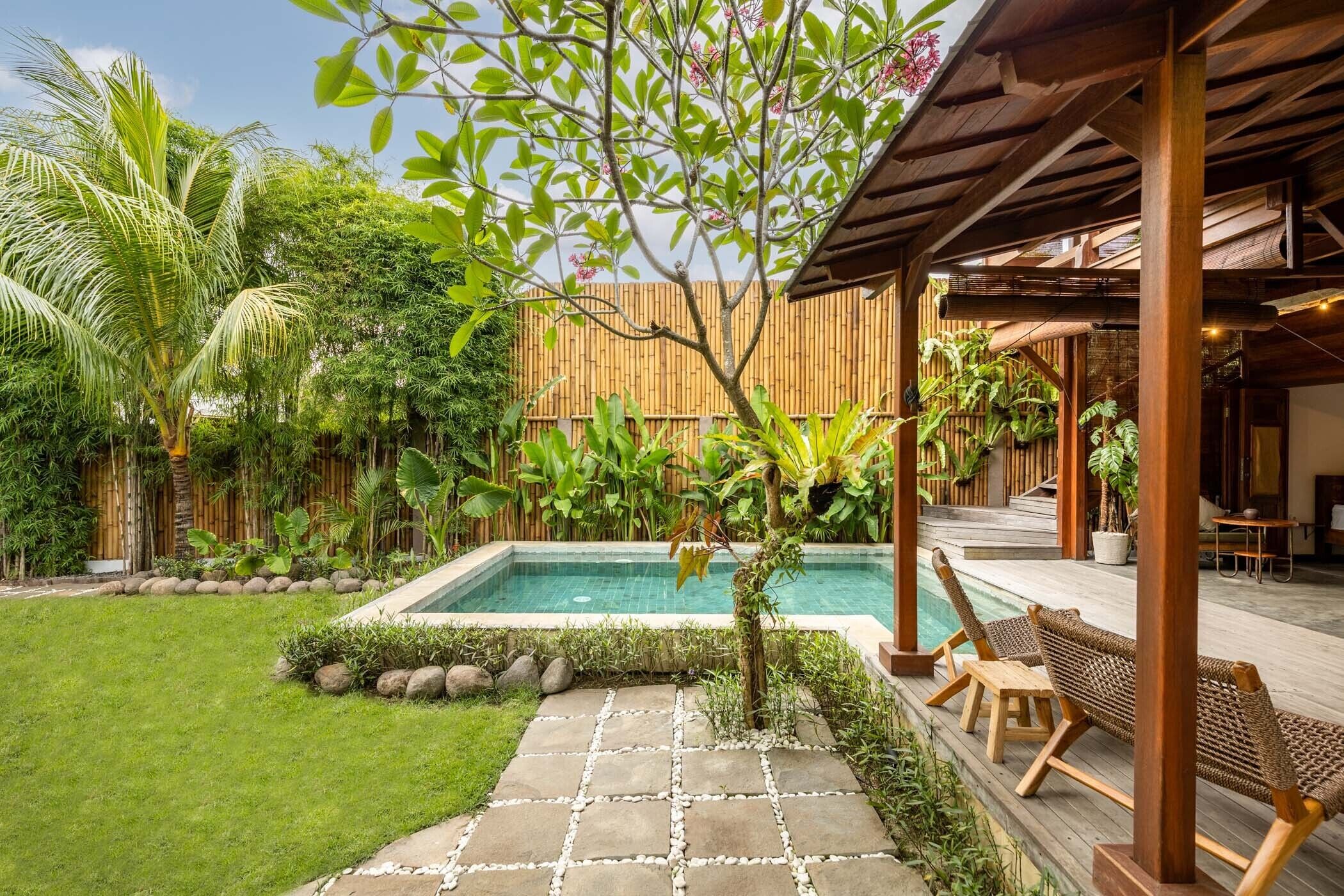 A poolside area with a wooden pergola, lounge chairs, and a bamboo fence.