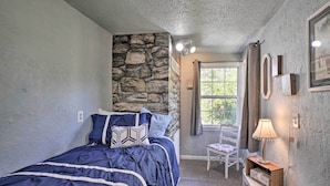 Un dormitorio con una pared de acento de piedra, una cama con colcha azul, una silla y una mesita de noche con lámpara.