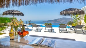 A poolside area with lounge chairs, umbrellas, and a view of the sea.