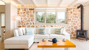 A modern living room with a white sofa, a wooden coffee table, a stone wall, and a wood-burning stove.