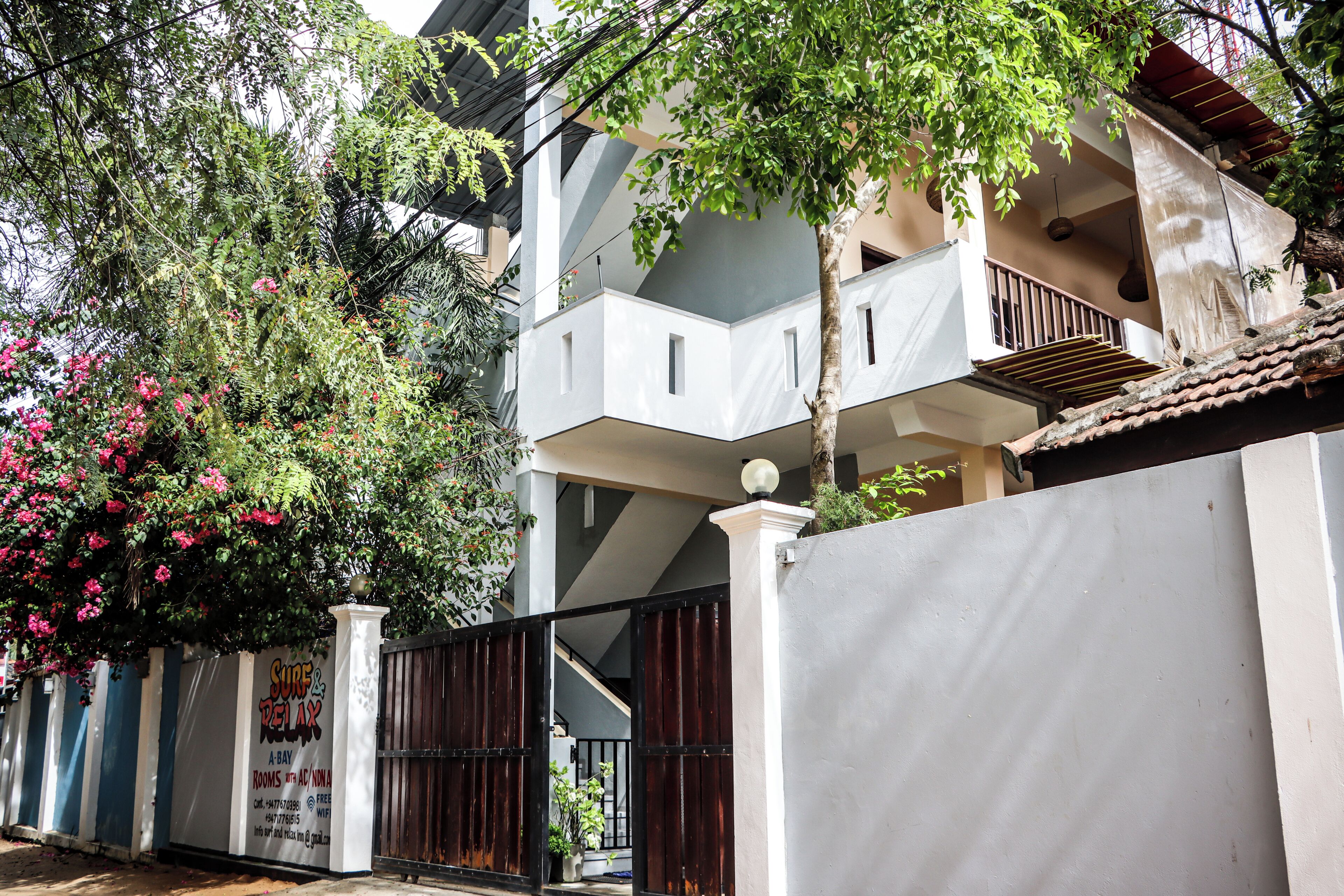 A multi-story building with balconies, a gated entrance, and a sign for 'Surf & Relax' rooms.