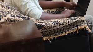 A person sitting on a patterned sofa using a laptop. - Surf & Relax Inn Arugambay (Arugam Bay)