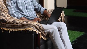 A person sitting on a patterned sofa with a laptop, in a room with a door and a green carpet. - Surf & Relax Inn Arugambay (Arugam Bay)