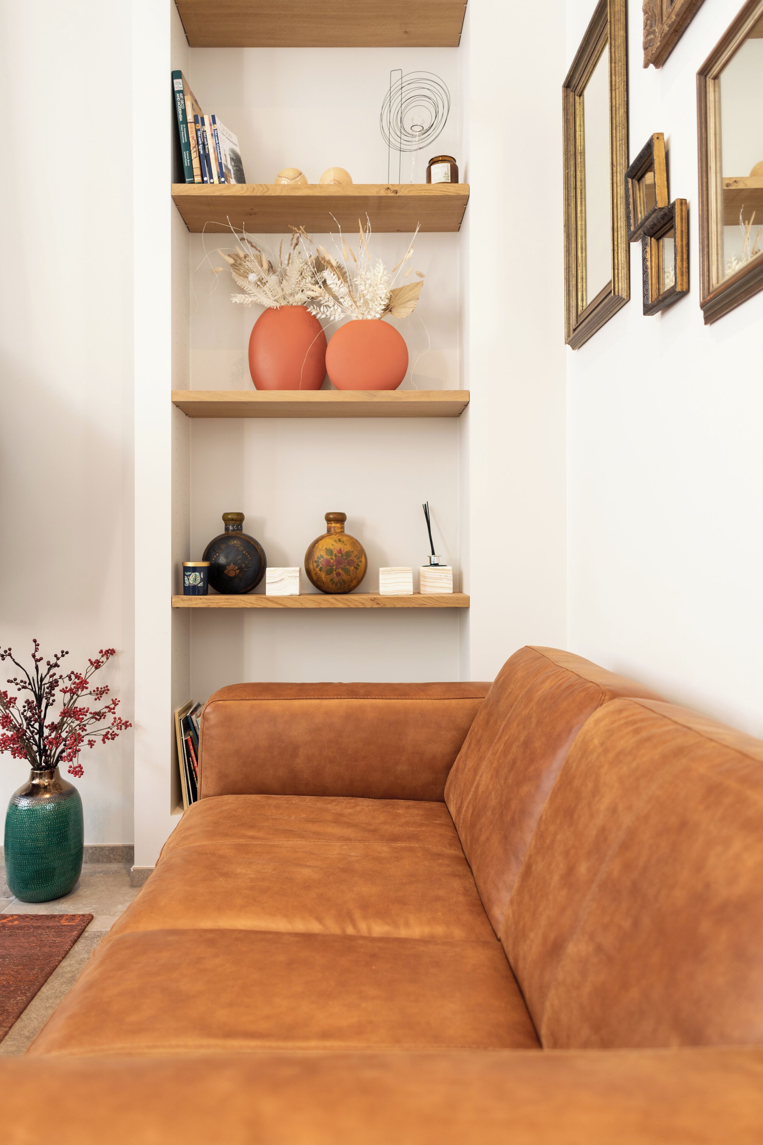 Ein braunes Ledersofa, Holzregale mit Dekoration und eine Vase mit getrockneten Pflanzen.