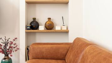 Ein braunes Ledersofa, Holzregale mit Dekoration und eine Vase mit getrockneten Pflanzen.
