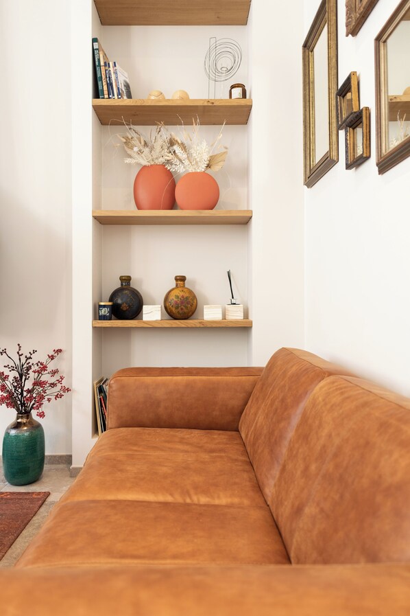 A brown leather sofa, wooden shelves with decorative items, and a vase with dried plants.