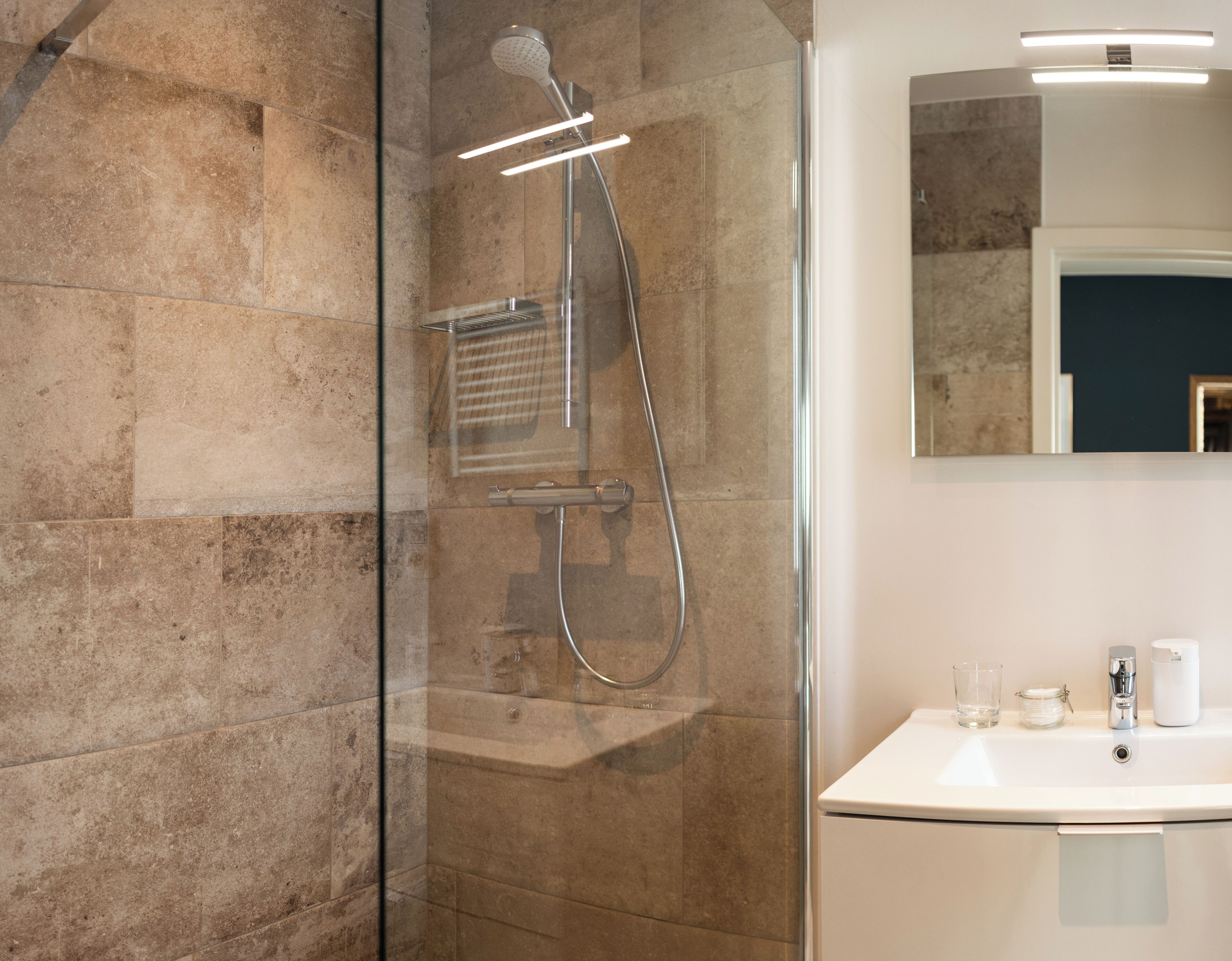 Un baño moderno con ducha envuelta en vidrio, un lavamanos blanco y un espejo sobre él.
