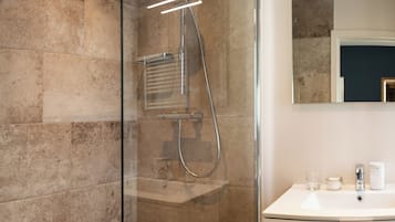 Un baño moderno con ducha envuelta en vidrio, un lavamanos blanco y un espejo sobre él.