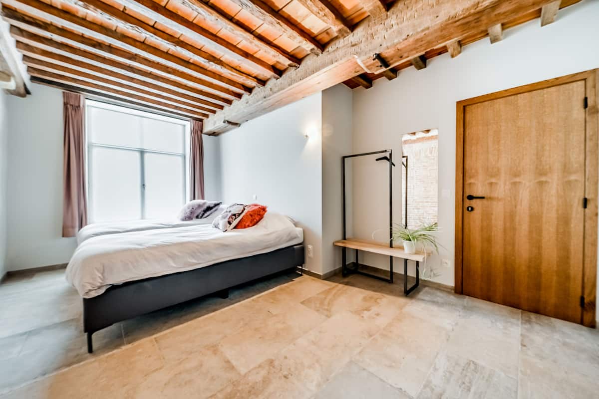 A bedroom with a bed, a bench, a door, and a window.