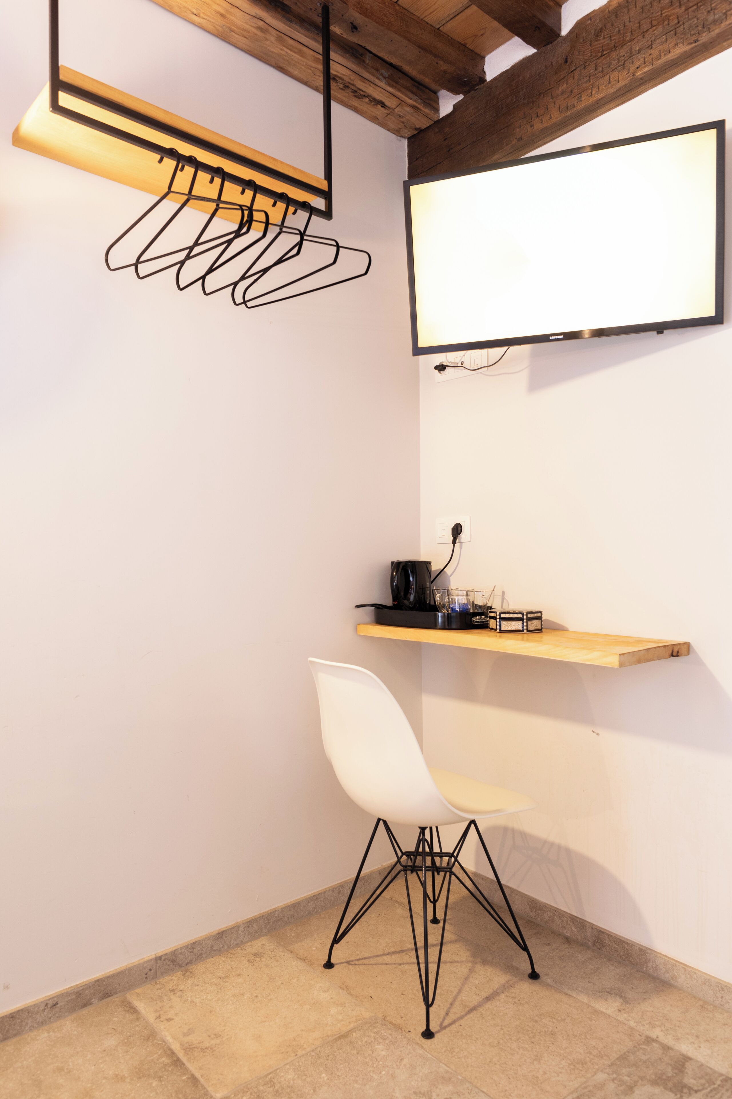 Una habitación moderna con una silla blanca, un estante de madera con una tetera y un televisor de pantalla plana.