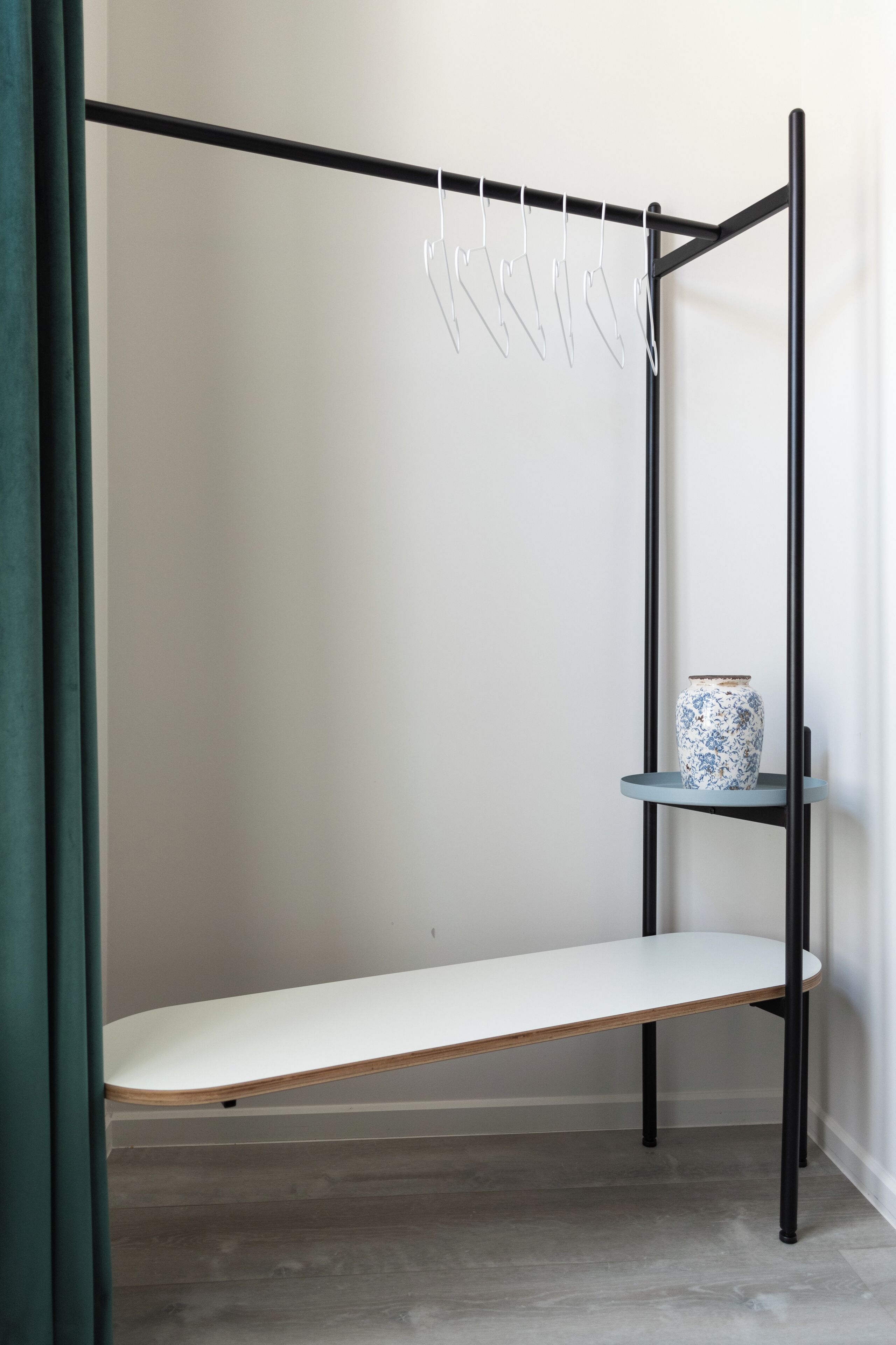 A minimalist room with a metal bed frame, a white bench, and a small shelf with a decorative vase.