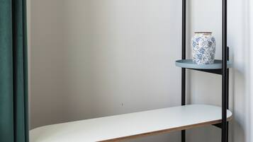 A minimalist room with a metal bed frame, a white bench, and a small shelf with a decorative vase.
