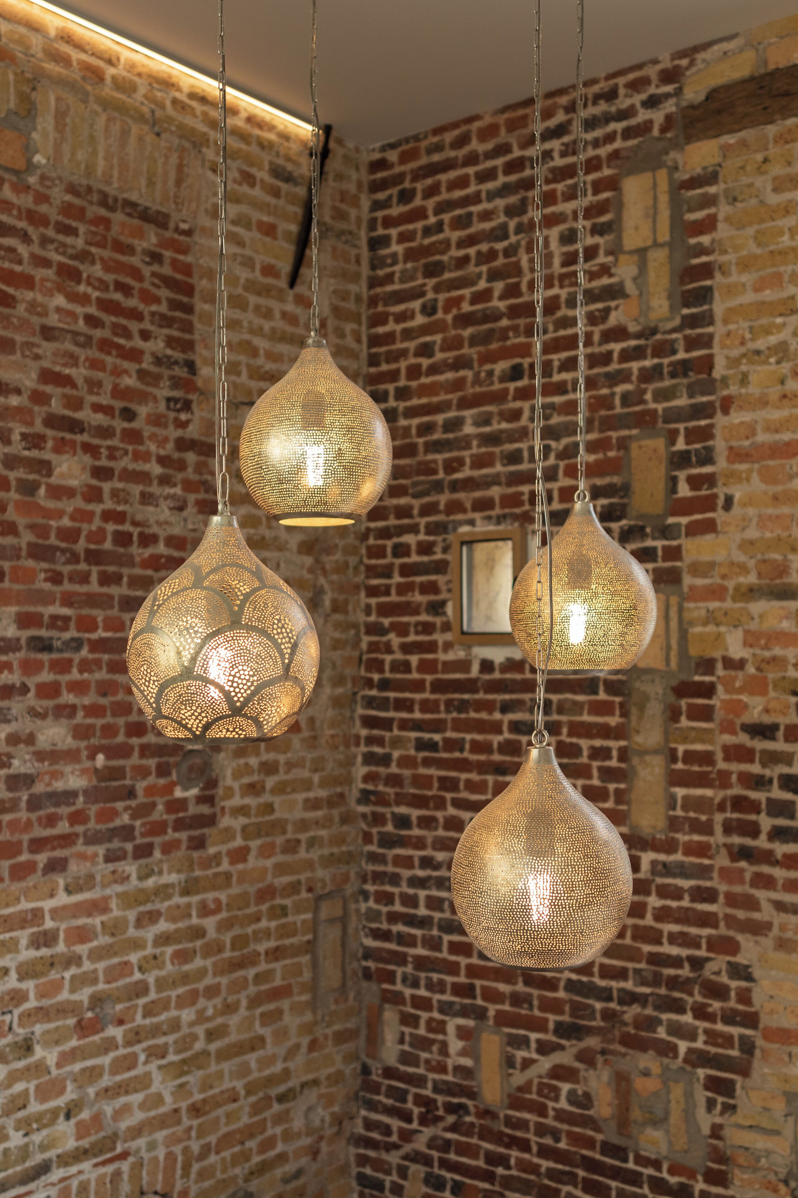 Drie hanglampen met ingewikkelde ontwerpen tegen een bakstenen muur.
