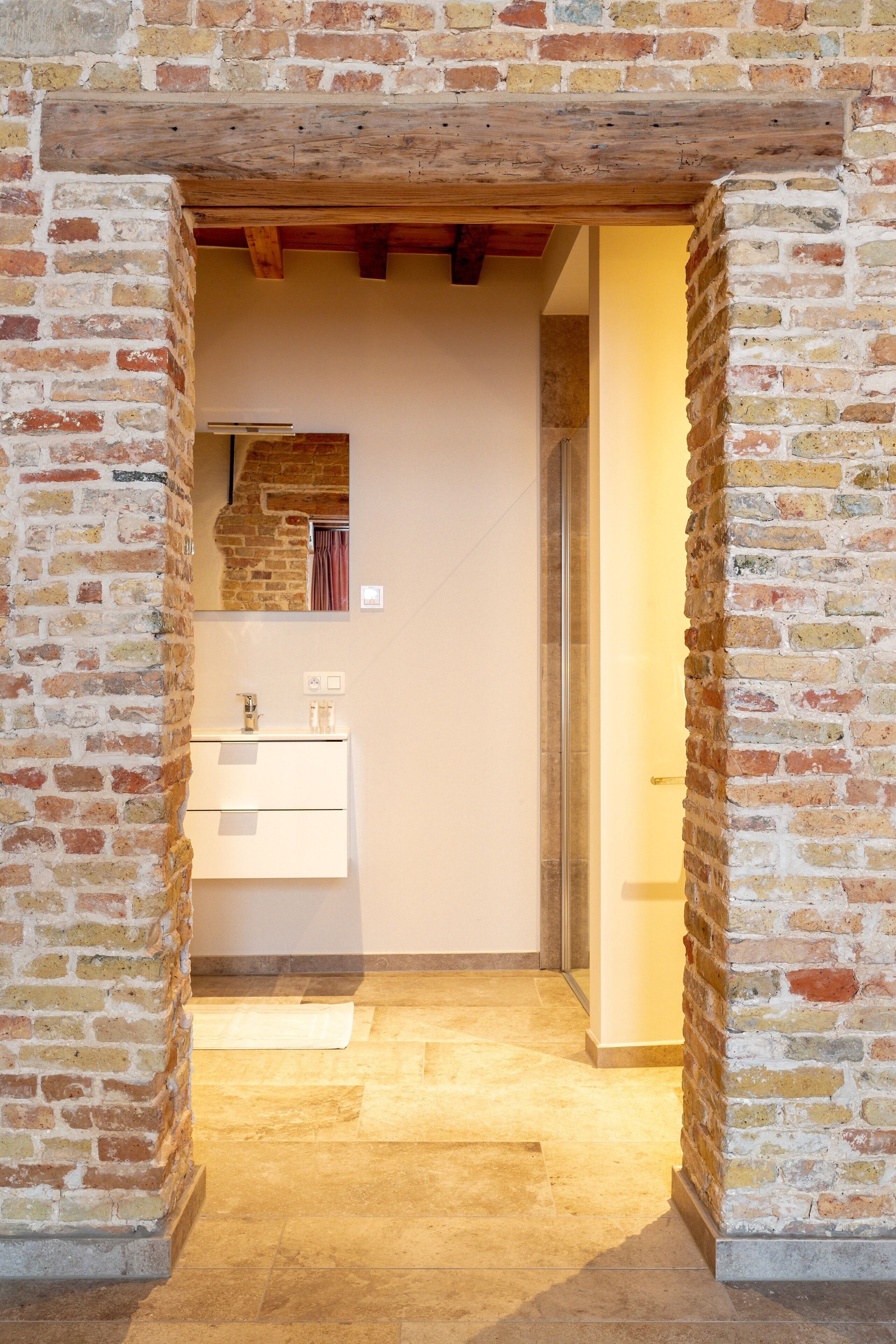 A narrow hallway with a brick wall, a wooden ceiling, and a glass shower enclosure.